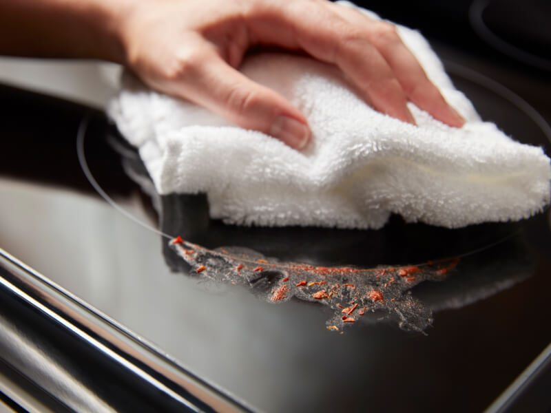 Person cleaning a mess on an electric cooktop