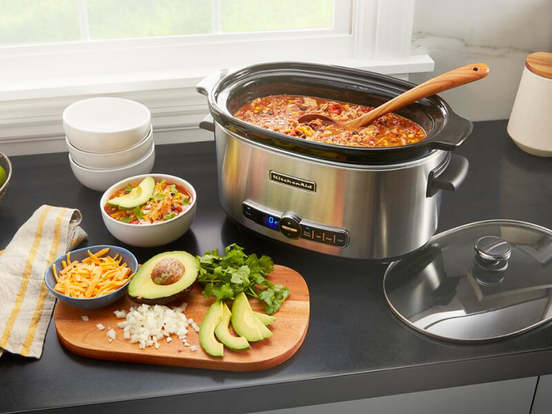 Slow cooker filled with chili next to a cutting board with toppings