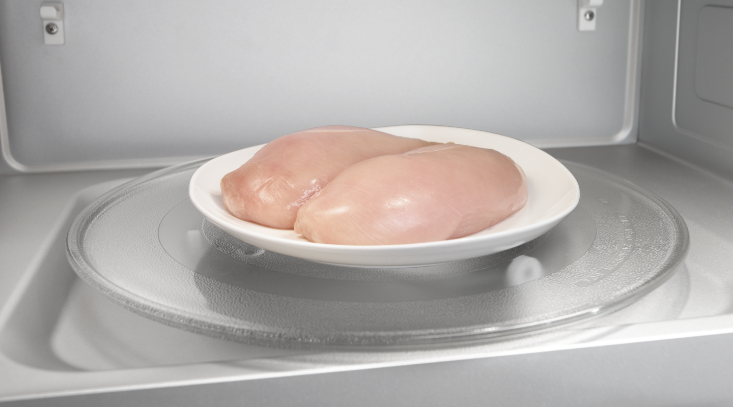 Two raw chicken breasts on a microwave-safe plate inside the microwave
