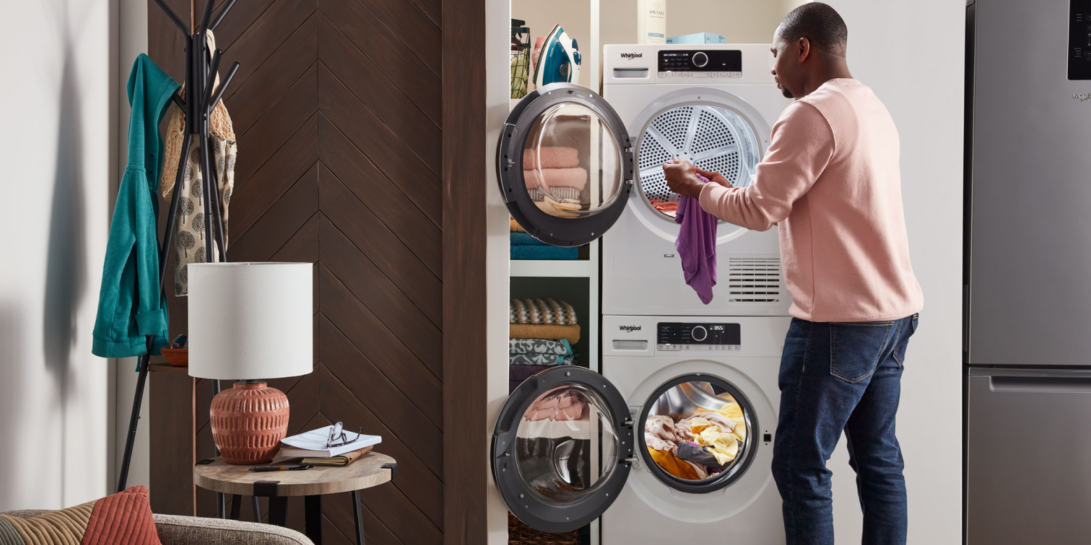 Man moving laundry from a stackable Whirlpool® front load washing machine down to the front load dryer below