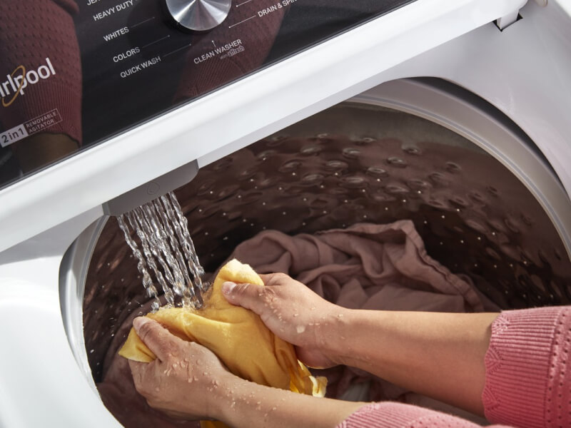 A person holding some laundry in the water stream of the washer as it fills