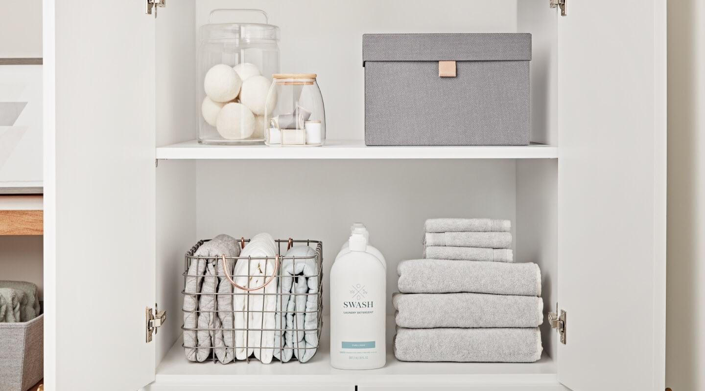 Swash® Laundry Detergent on the bottom shelf of a white cabinet between stacks of gray towels