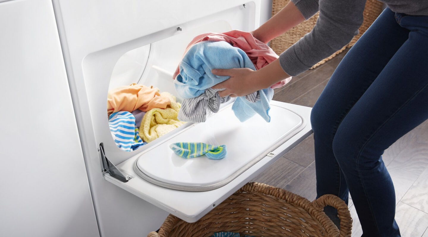 Person removing dry clothes from a dryer and placing them in a basket