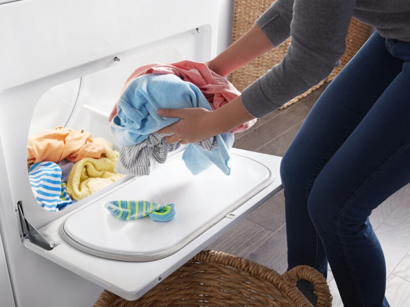 Person removing dry clothes from a dryer and placing them in a basket