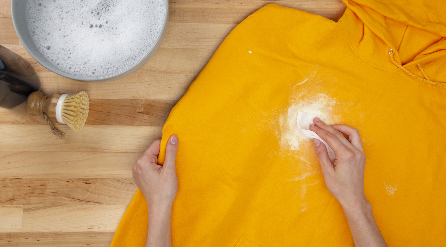 Hand blotting white paint on a yellow sweatshirt with a paper towel