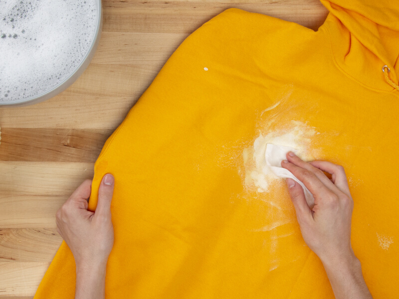 Hand blotting white paint on a yellow sweatshirt with a paper towel