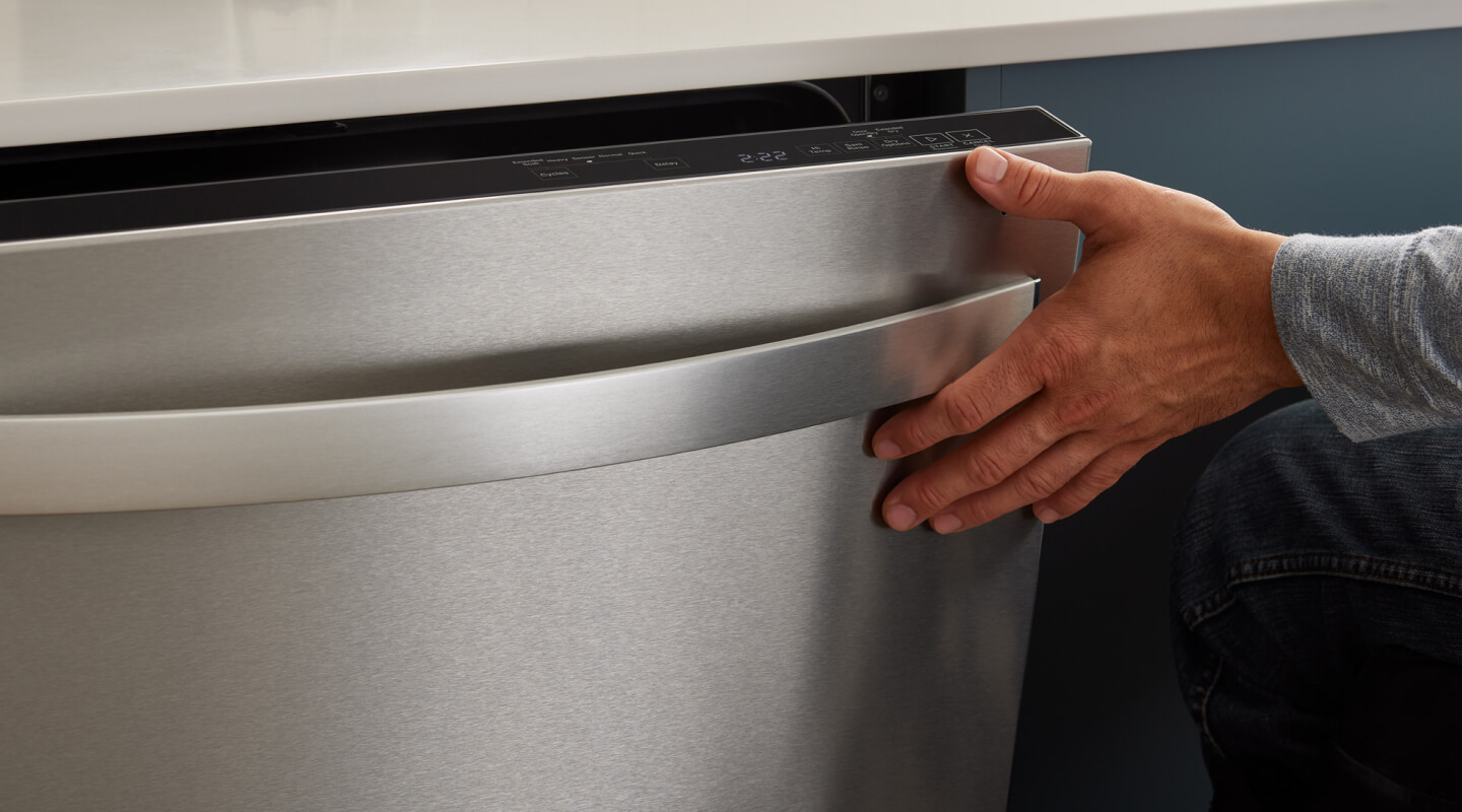 A close up of a hand closing a dishwasher door