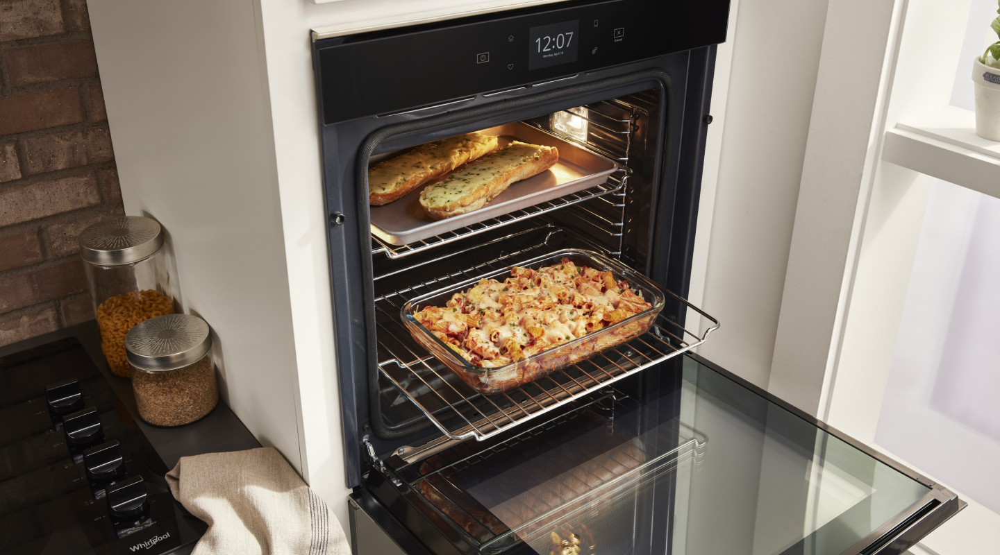 Open Whirlpool®  single wall oven showing a tray of garlic bread and casserole dish