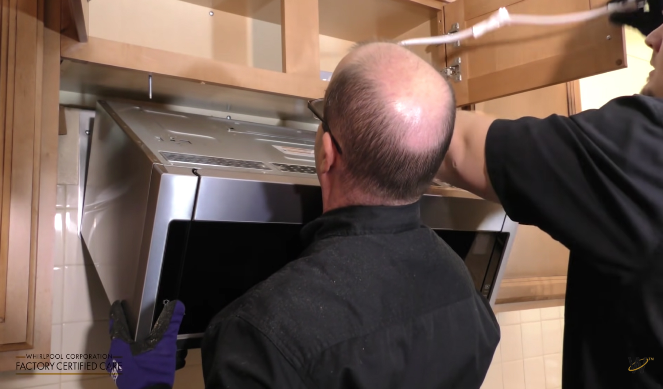 Two people lifting and aligning the microwave oven into place