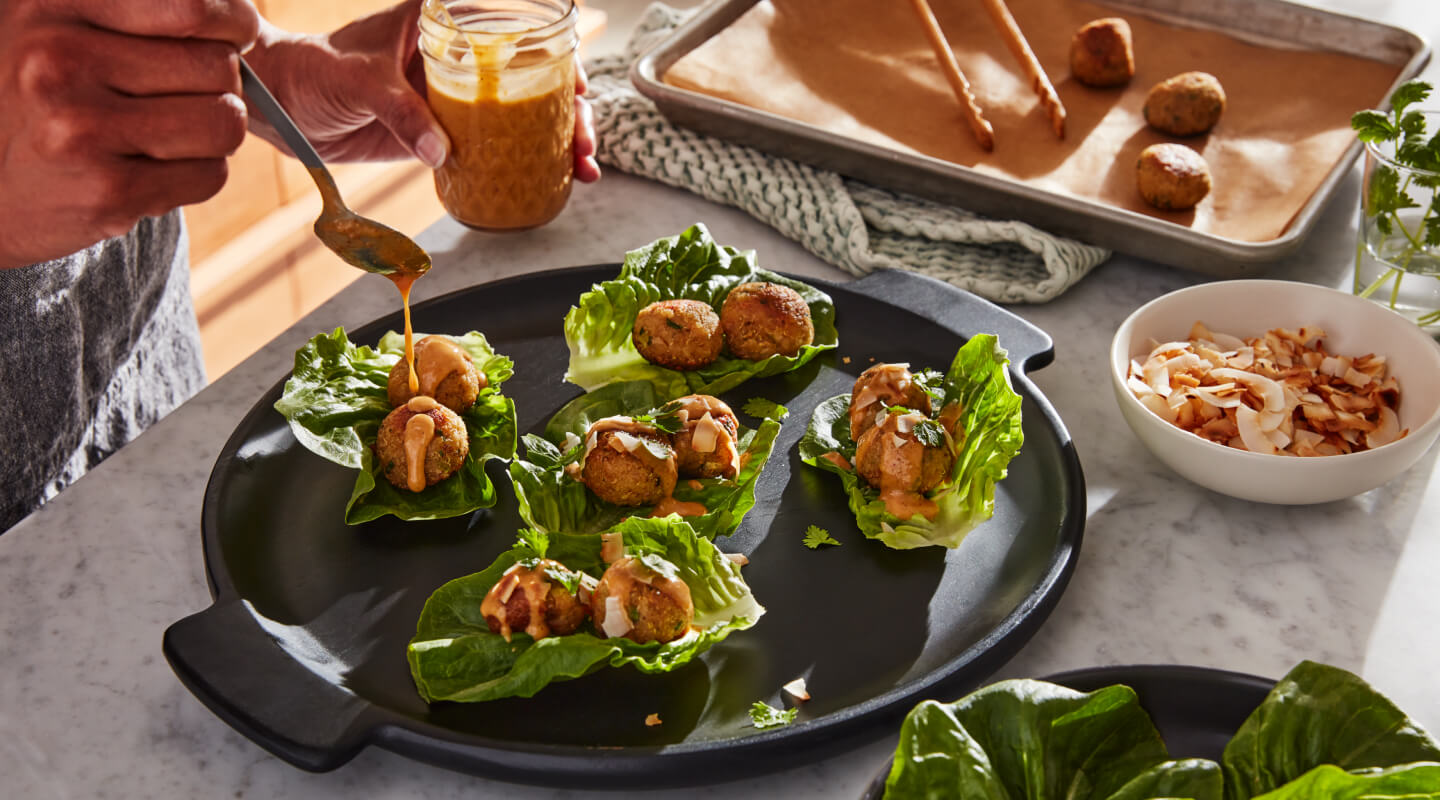 Person topping lettuce wraps with sauce