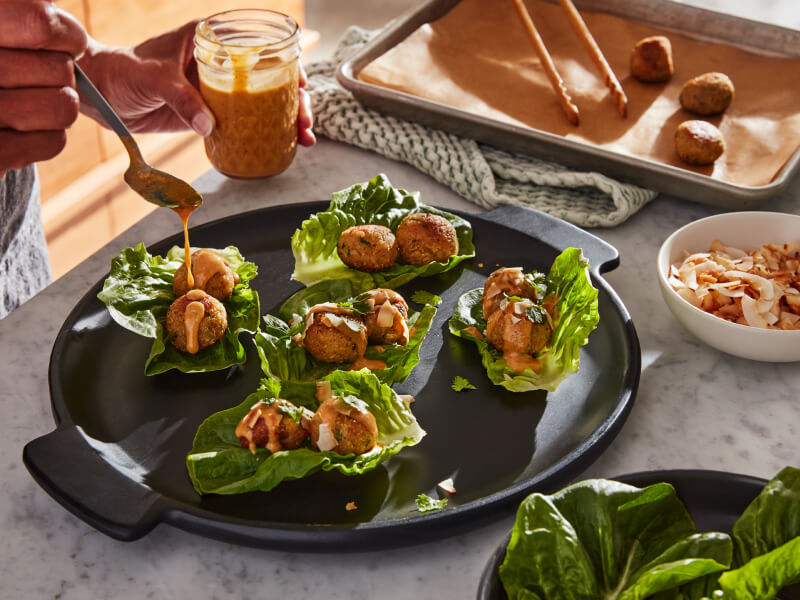 Person topping lettuce wraps with sauce
