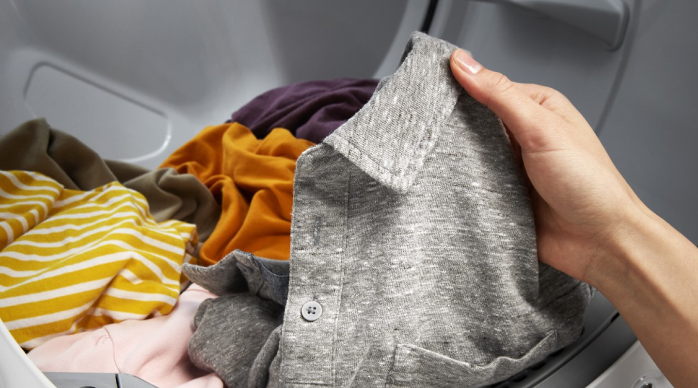 A person pulling a gray polo out of a washer.
