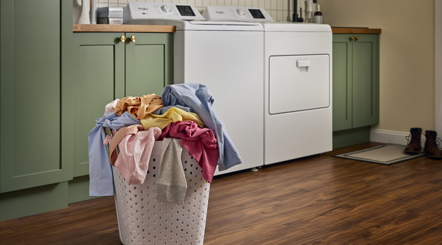 Clothes in a basket in front of a white Whirlpool® Washer and Dryer
