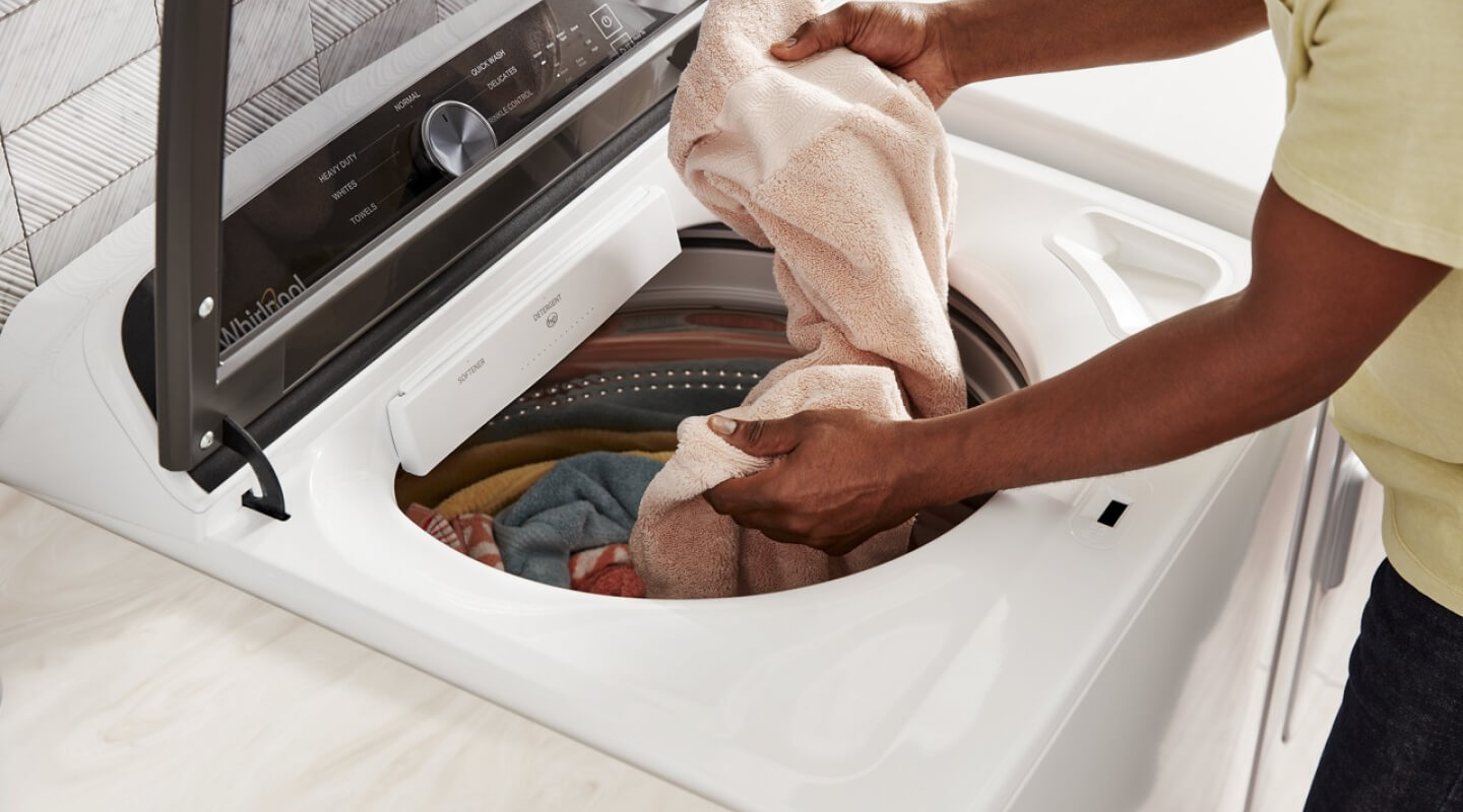 A person putting laundry into a white Whirlpool® Washing Machine
