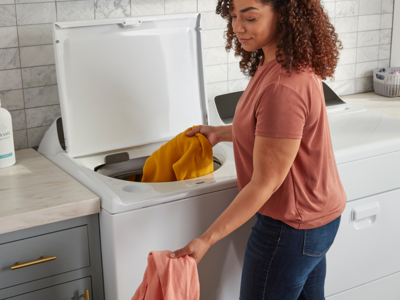 A woman puts clothes into a washer