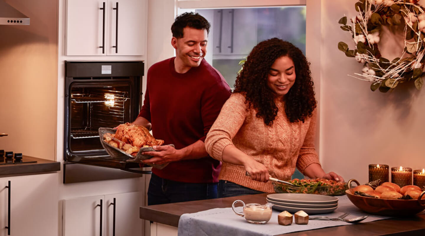 A couple preparing a dinner of roasted chicken, vegetables and bread rolls