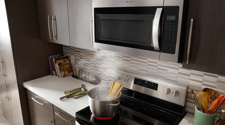 An over-the-range microwave with a pot of pasta cooking on the stove below