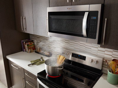 An over-the-range microwave with a pot of pasta cooking on the stove below