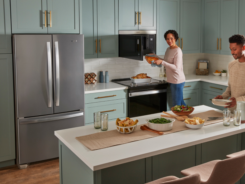 Two people cooking and preparing a meal in a kitchen with blue cabinets and white backsplash. 