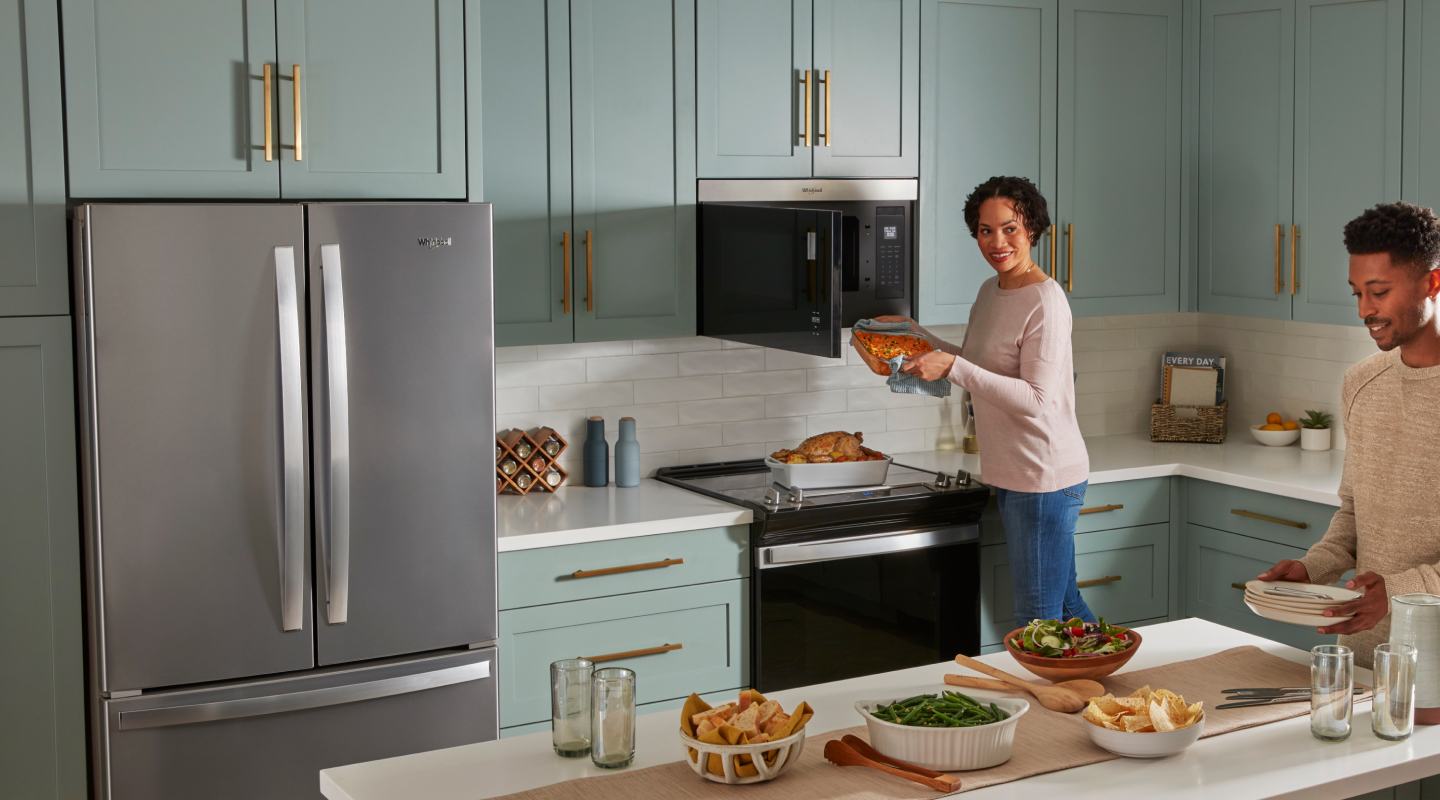 Two people cooking and preparing a meal in a kitchen with blue cabinets and white backsplash. 