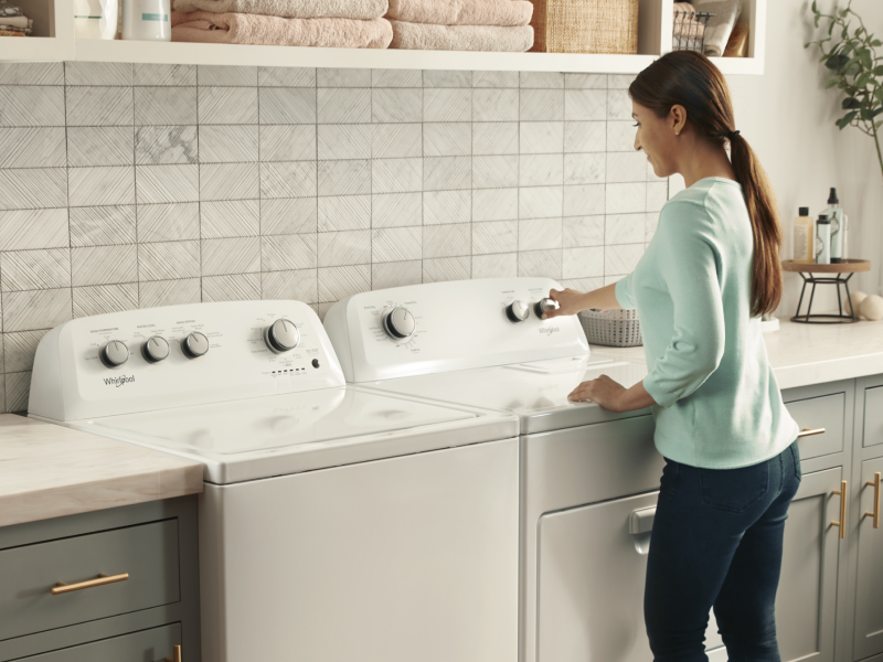 A woman using a Whirlpool® dryer next to a matching washer