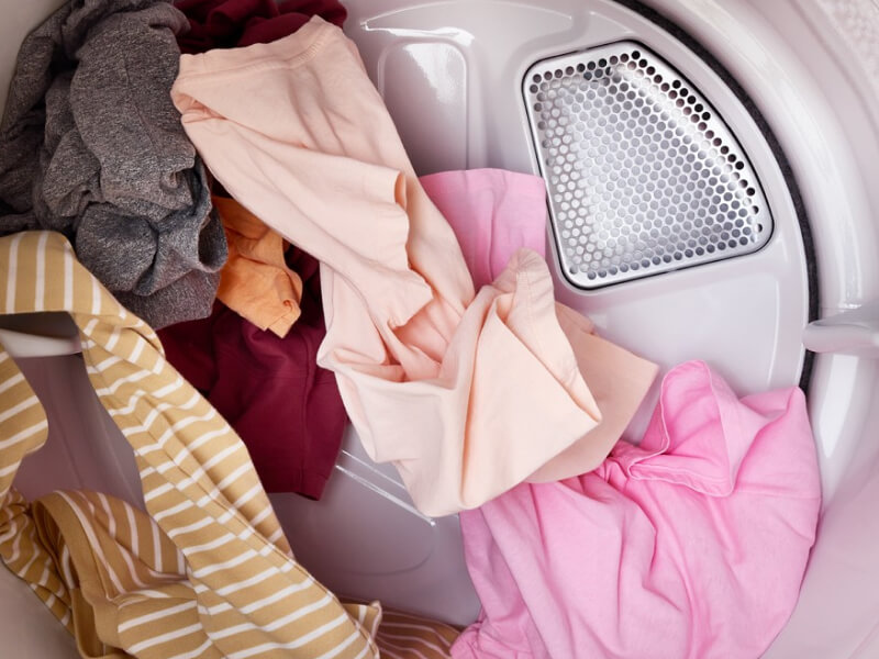 Yellow striped, gray and pink clothes tumbling in a dryer