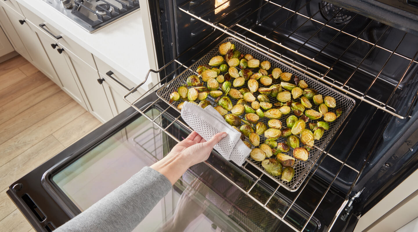 A person removing a tray of Brussels sprouts from an oven