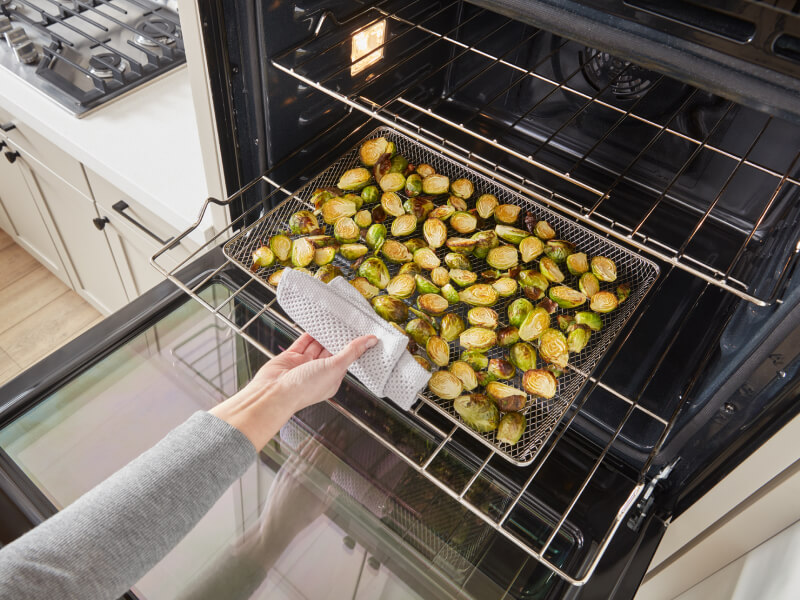 A person removing a tray of Brussels sprouts from an oven