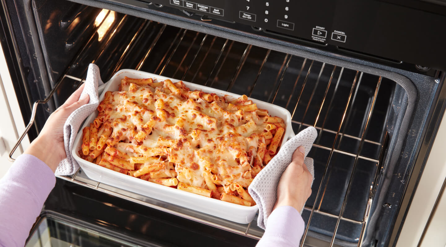 A person removing a dish of baked ziti from an oven
