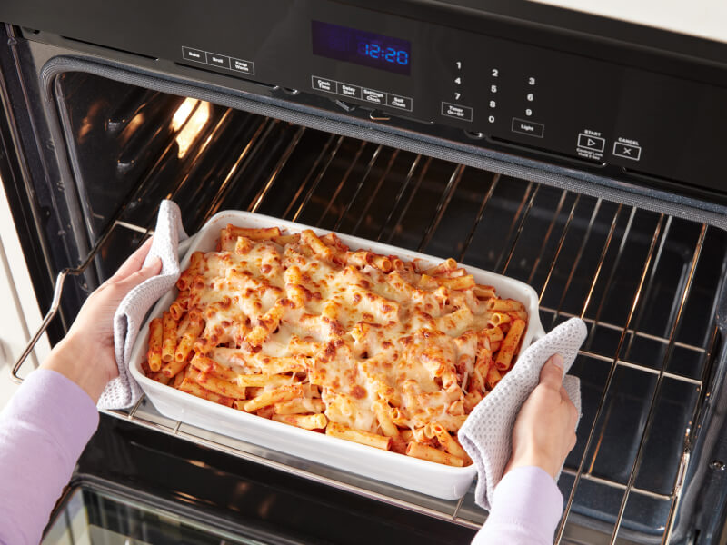 A person removing a dish of baked ziti from an oven