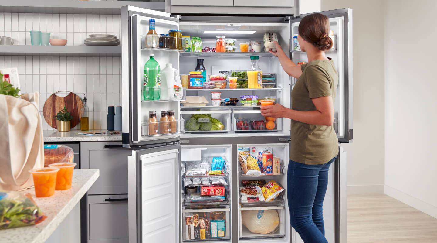 A person putting food in her open refrigerator