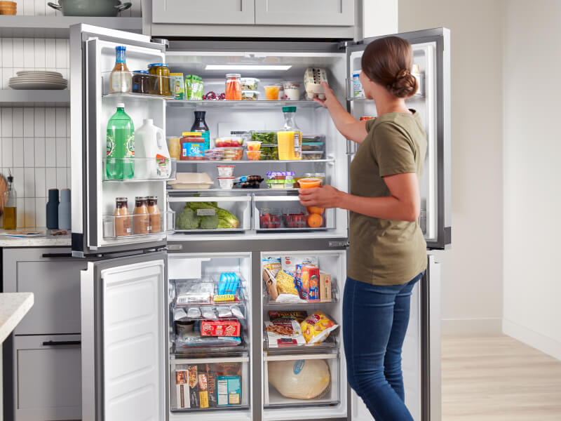 A person putting food in her open refrigerator
