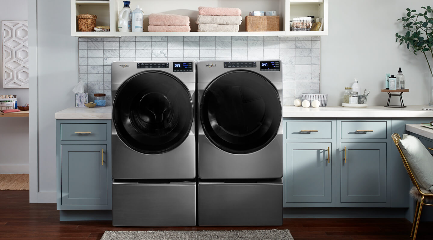 Gray Whirlpool® Front Load Washer and Dryer Pair on pedestals in blue cabinetry