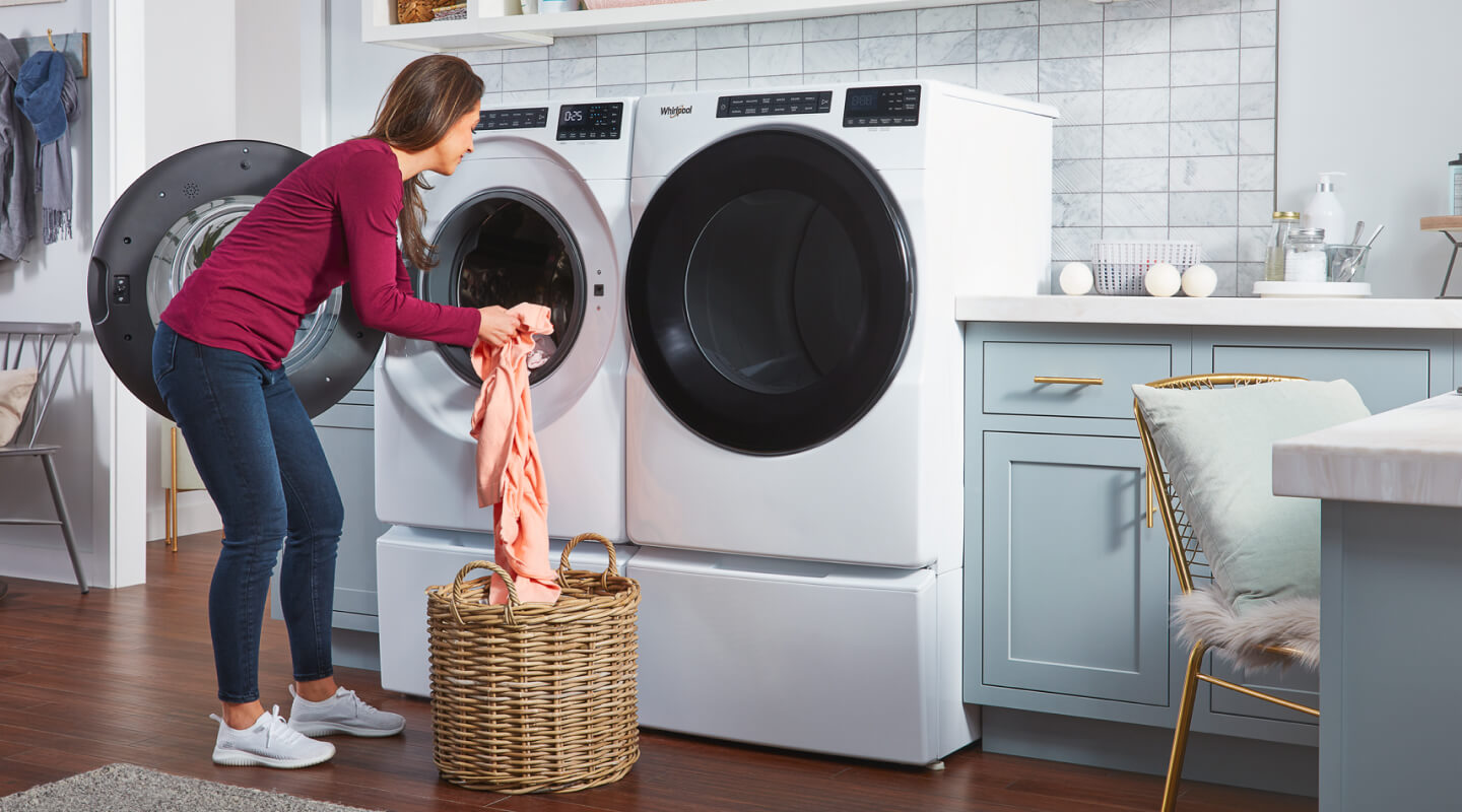 Person transferring laundry from a wicker basket into a white front load washer