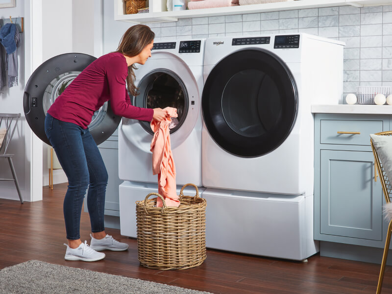 Person transferring laundry from a wicker basket into a white front load washer