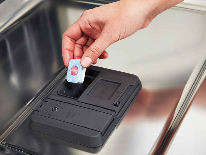 Person placing dishwasher pod into detergent dispenser