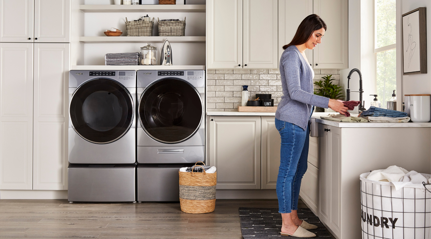 Woman in a laundry room with stainless steel Whirlpool® front load washer and dryer set