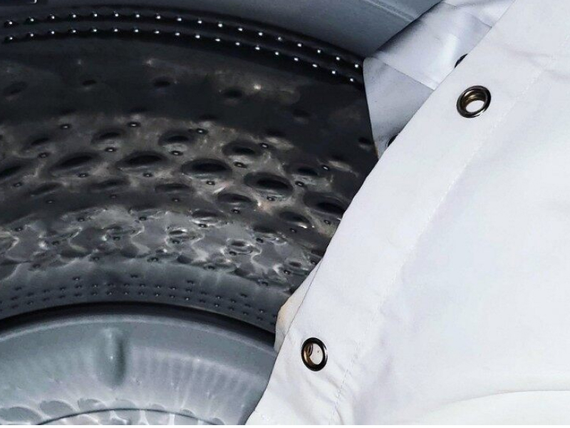 A white shower curtain being placed in a washer.