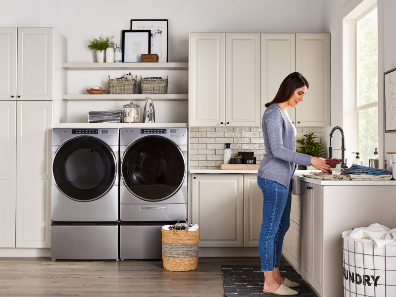 A person folding laundry with a Whirlpool® washer and dryer nearby.
