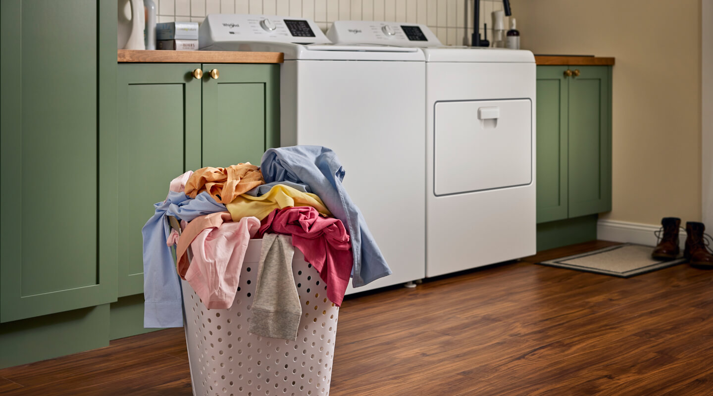 Laundry basket full of laundry in front of top load washer and dryer