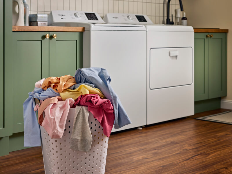 Laundry basket full of laundry in front of top load washer and dryer