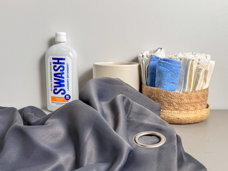 Grey curtains near a bottle of Swash® Laundry Detergent