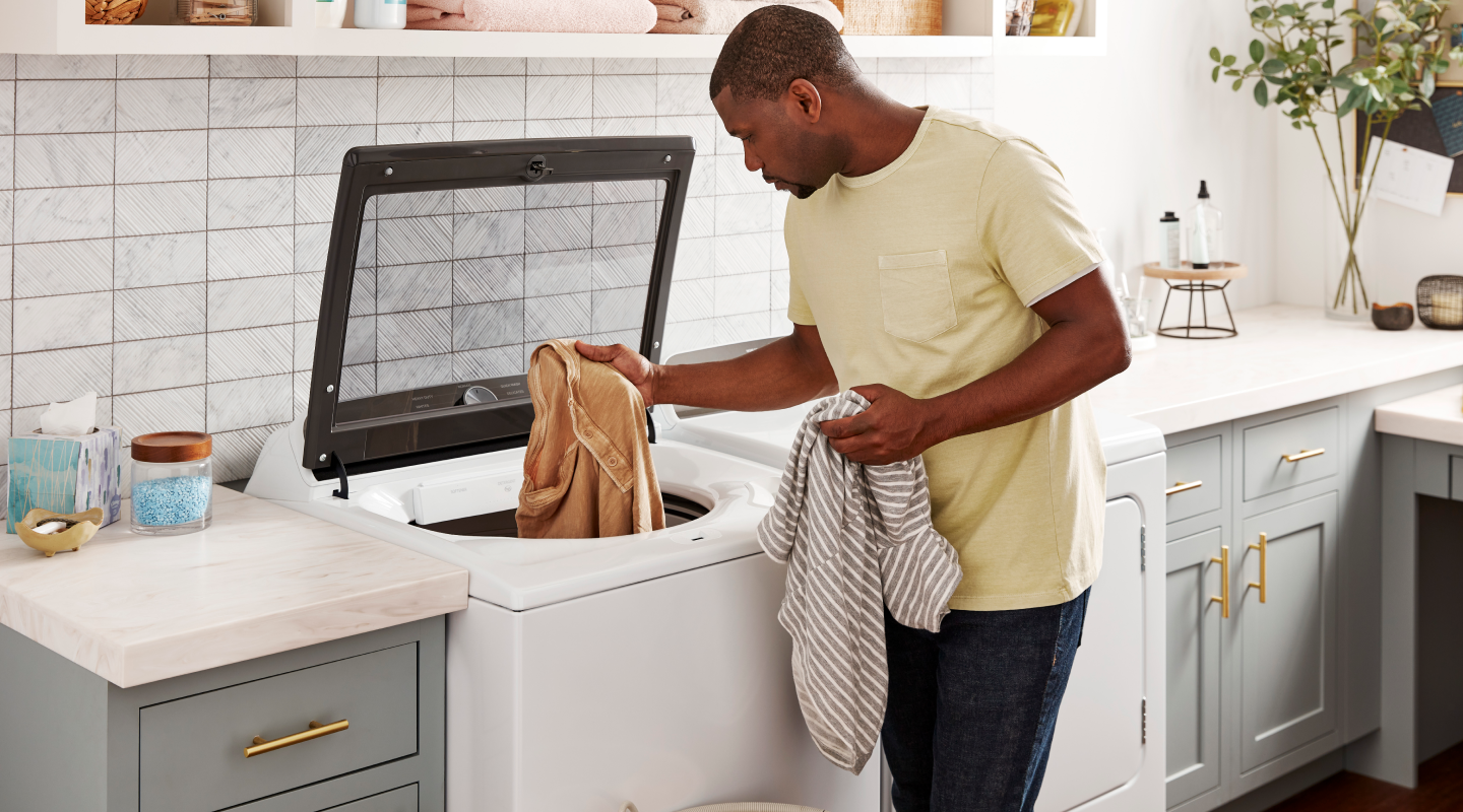 A man loading a top-load washer with clothes
