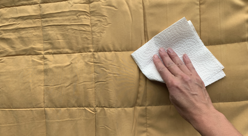 Person patting weighted blanket with a paper towel