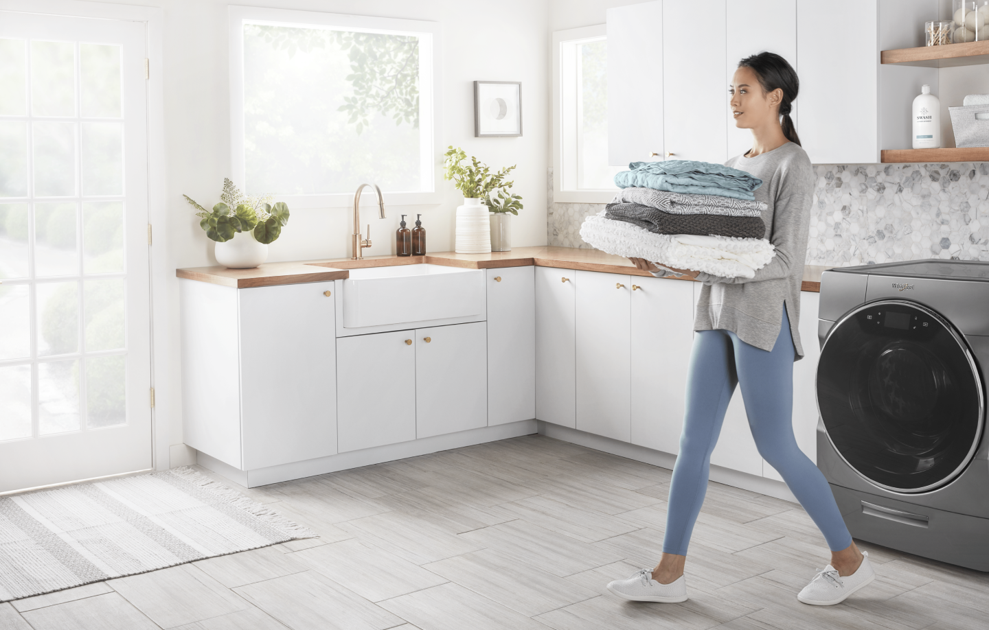A woman carrying folded laundry cleaned by a Whirlpool® washing machine