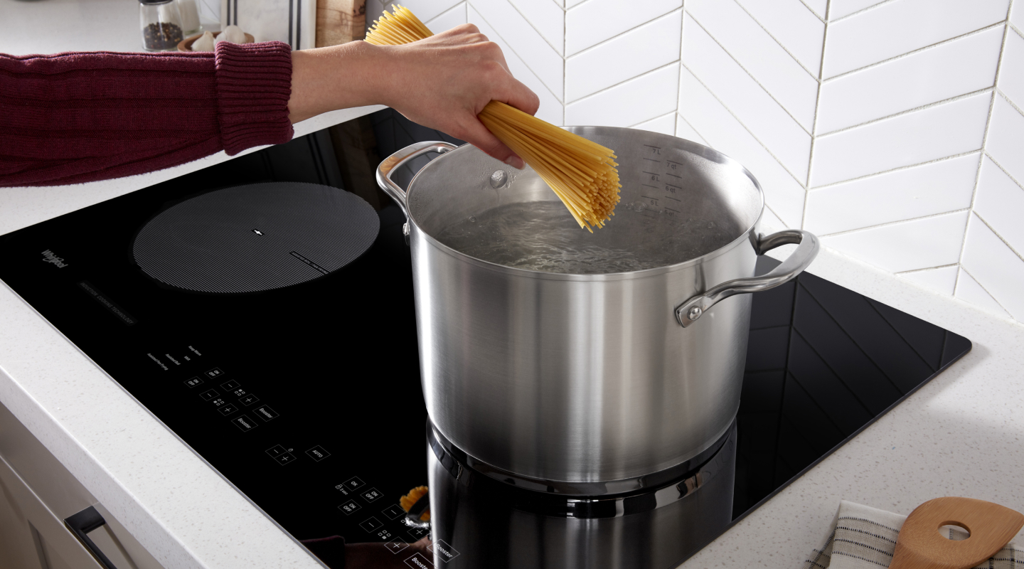 Person adding spaghetti to a stock pot on an induction cooktop