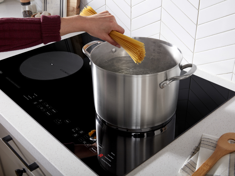 Person adding spaghetti to a stock pot on an induction cooktop