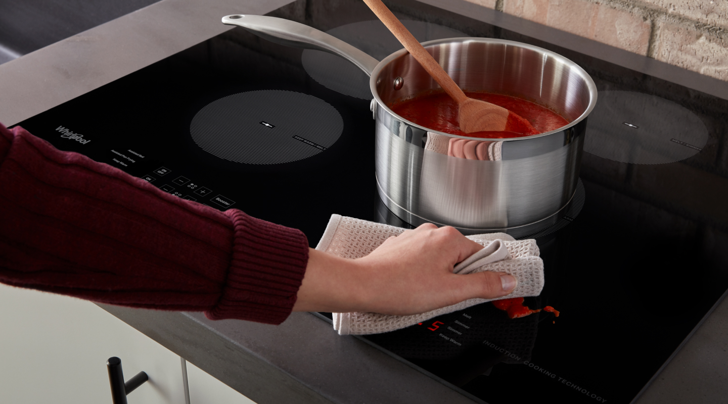 Person wiping sauce splatter off of an induction stovetop