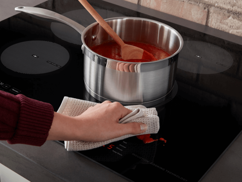 Person wiping sauce splatter off of an induction stovetop