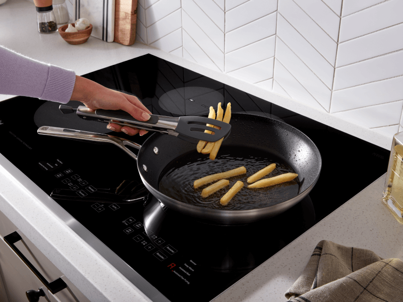 Person frying french fries in a frying pan on top of an induction cooktop